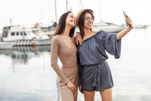 Two women tourist take a selfie on the phone at the yacht club. Travel concept. Spend time together