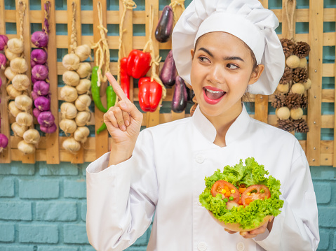 Asian woman in chef's uniform is cooking in the kitchen. portrait female cook smiling with copy space.