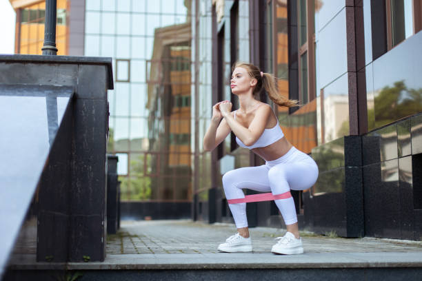 молодая подтянутая женщина тренирует мышцы ног с помощью фитнес-резинок в городе. тренировка на свежем воздухе - rubber band стоковые фото и изображения