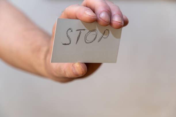 istock Stop. A word written in jagged letters. A man's hand holds a white paper rectangle with text against a gray background. 1396401690