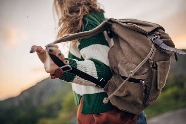 One woman, young female hiker standing high on mountain in sunset, she is taking of her backpack.
