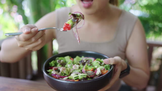 Hungry Asian woman having greek salad as her lunch