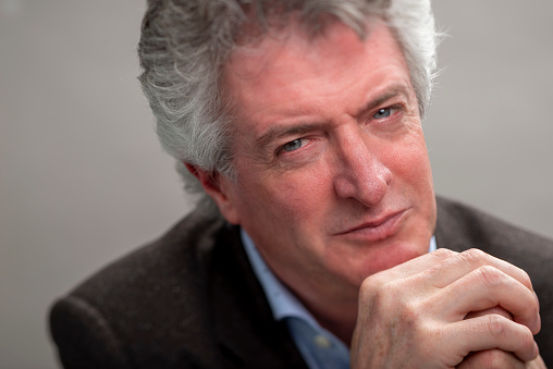 Portrait of real man with gray hair looking confident straight in the camera on gray background with a serious look, selective focus.