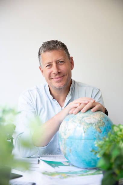 istock Business portrait of environmental engineer sitting by his work table holding globe in his hands and surrounded by plants 1396402907