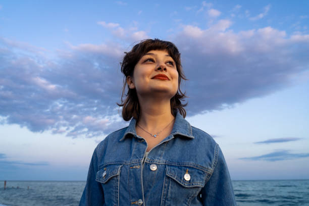 Look to the future with hope! Photograph of a beautiful young woman wearing a denim jacket and smiling towards the sun, taken in the sweet pastel colors of the sunset. hope stock pictures, royalty-free photos & images