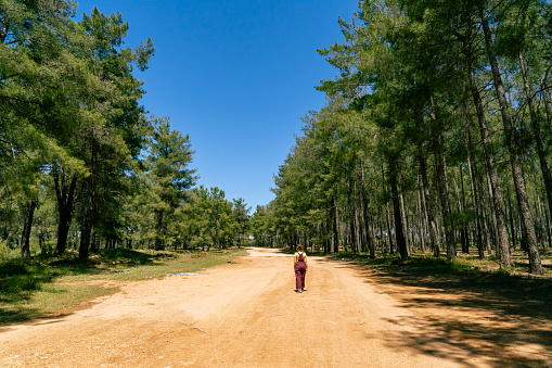 A young woman taking a walk on the dirt road deep into the forest