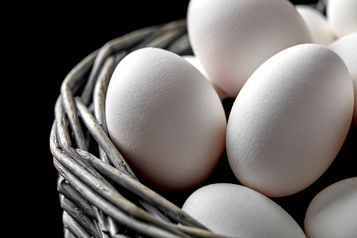 Basket filled with white eggs on black background
