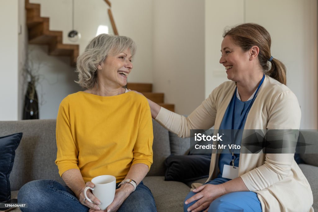 A nurse conducts an interview with a patient at home in a happy mood over coffee. A Latin doctor and nurse conducts an interview with a patient at home in a happy mood over coffee. Home Caregiver Stock Photo