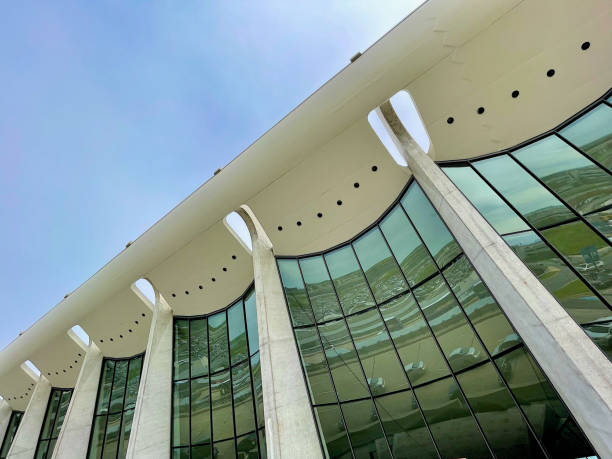Dulles, Virginia, USA - May 8, 2022: Cars are reflected in the glass facade between the supports for the catenary curve ceiling of the iconic main terminal on a sunny afternoon.