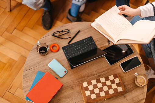 High angle view of a coffee table during the meeting with the office supplies and chess board while an employee is holding a notebook