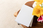 White book blank cover mockup on stylish wooden coffee table with tulips bouquet, high angle view