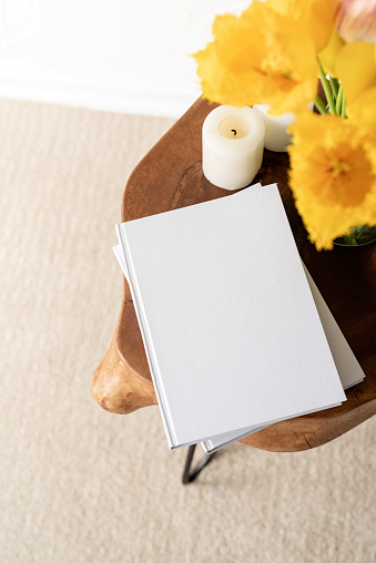 White book blank cover mockup on stylish wooden coffee table with tulips bouquet, high angle view. Mock up design