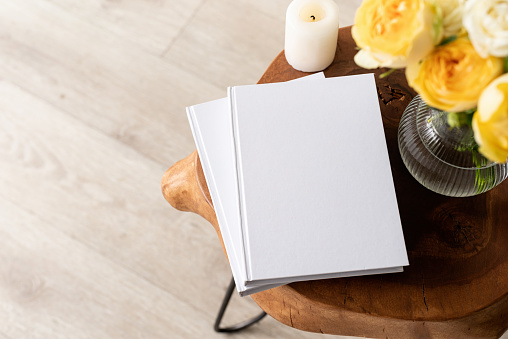 White book blank cover mockup on stylish wooden coffee table with roses bouquet, high angle view. Mock up design