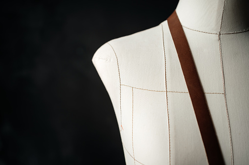 Tailor Mannequin with measure tape in front of wooden wall.