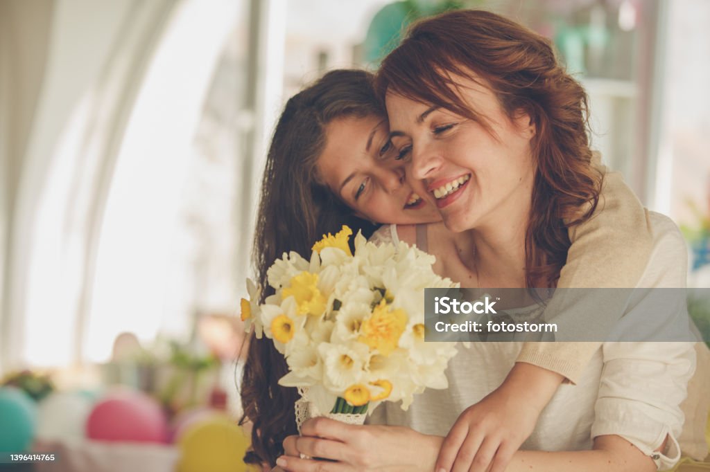 Cheerful woman getting a bouquet of yellow daffodils from her daughter for Mother's day Copy space shot of a cheerful mid adult woman smiling after her young daughter, who is embracing her from behind, surprised her with a bouquet of yellow daffodils for Mother's day. Mother's Day Stock Photo