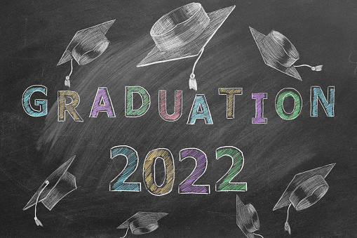 Hand drawn text GRADUATION 2022 and graduation caps on blackboard.