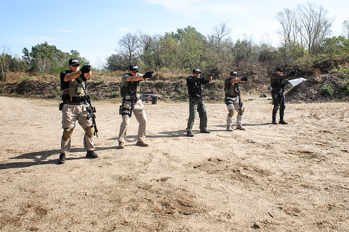 Group of army soldiers practice gun shooting on target on outdoor shooting range. Firearm shooting and tactical training