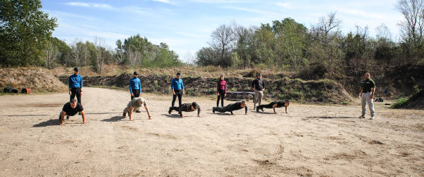 Two athletic men doing outdoor functional workout exercises on autumn grass with fallen leaves, smiling and enjoying fitness training