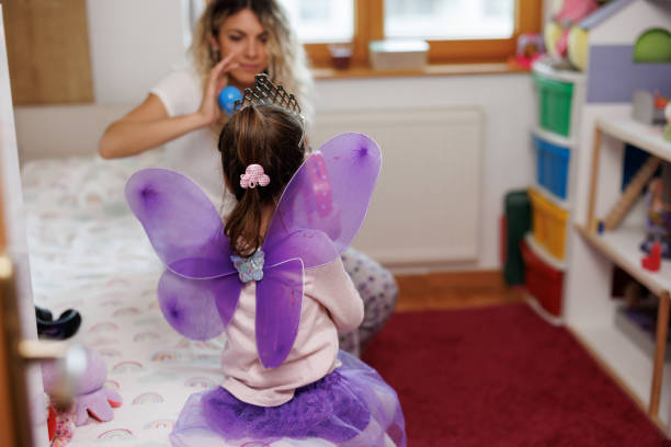 Young mother and cute little daughter with purple fairy wings playing at home