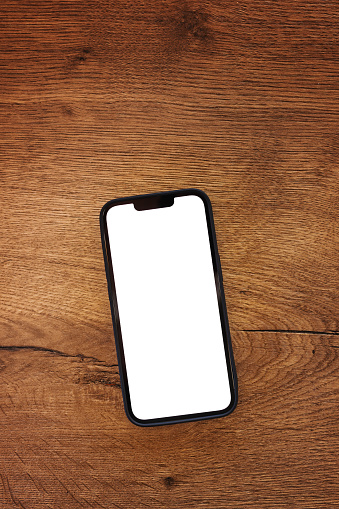 Smartphone with blank white mockup touchscreen on teak wooden table, top view