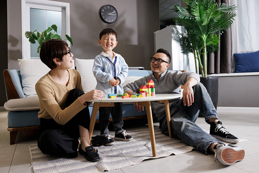 Young asian parents, indoors during the day, play with their son on building blocks.