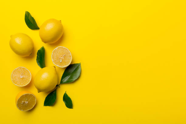 istock Many fresh ripe lemons with green leaves on colored background, top view, space for text 1396427659