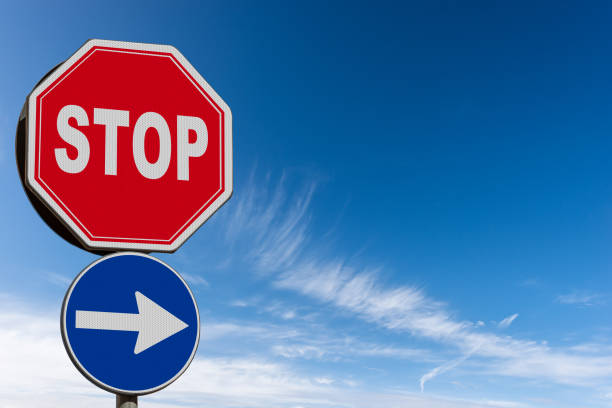 Close-up of an one way and a stop road sign against a clear blue sky with clouds and copy space. Italy, Europe.