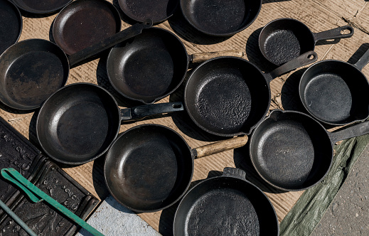 Many vintage empty cast-iron frying pans on floor of market. Top view