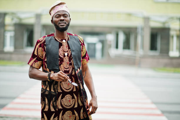 uomo africano elegante e bello in abito tradizionale e berretto in piedi all'aperto. - nigerian culture men africa african culture foto e immagini stock