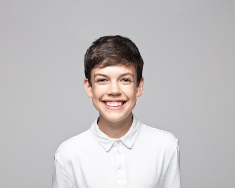 Portrait of cheerful teenage boy standing against gray background.