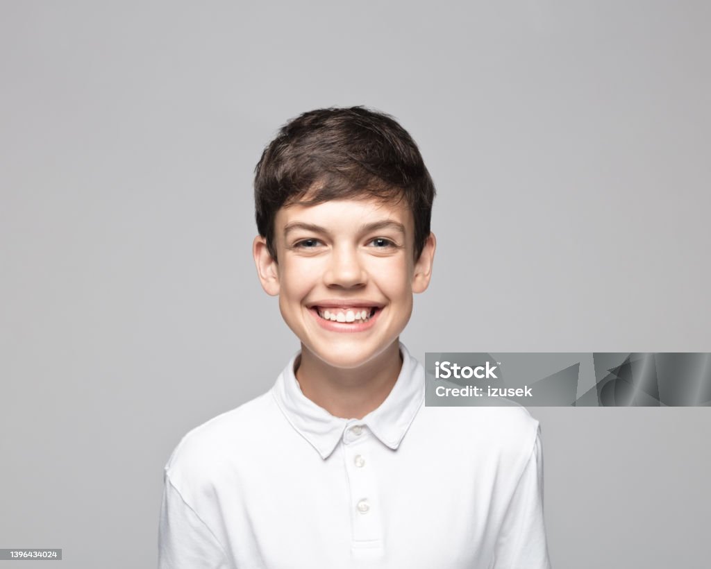Happy teenage boy against gray background Portrait of cheerful teenage boy standing against gray background. Teenage Boys Stock Photo