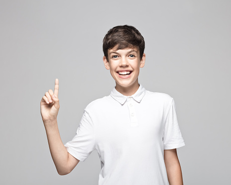 Portrait of happy teenage boy pointing while standing against gray background.