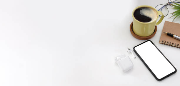 Smart phone, coffee cup, notebook and wireless earphone on white table. Top view, copy space.