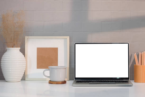 istock Stylish workplace with computer laptop, picture frame, coffee cup and flower pot on white table. 1396434827