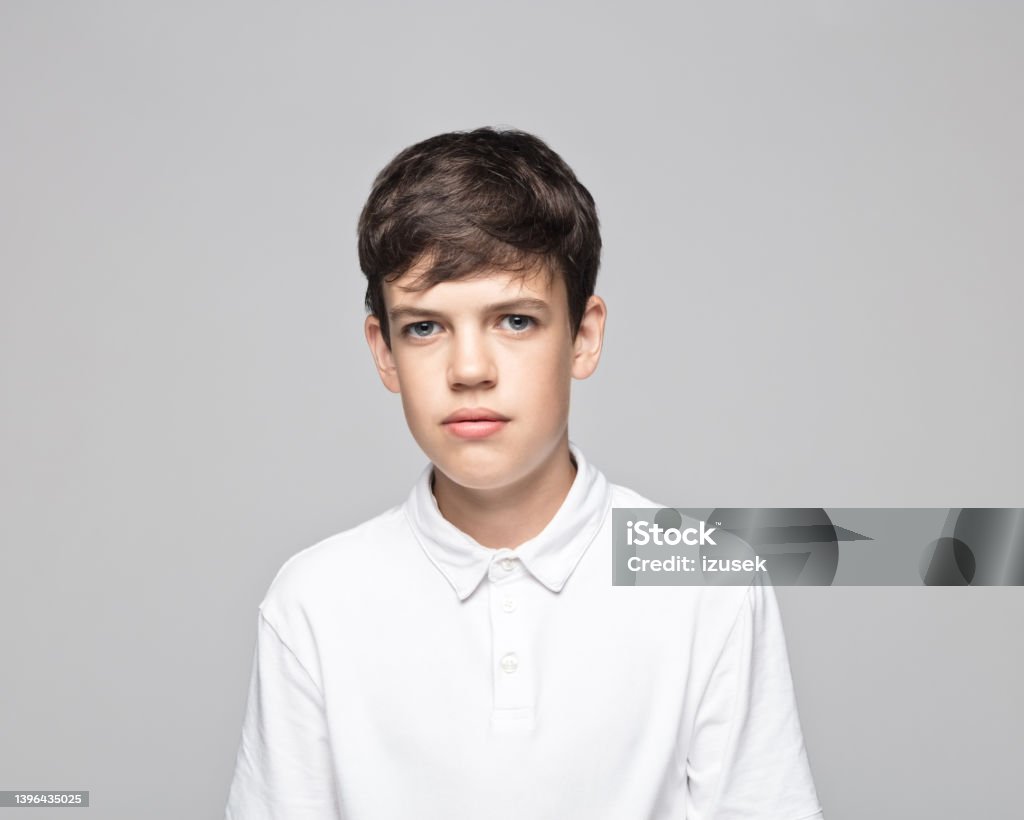 Sad teenage boy against gray background Portrait of sad teenage boy wearing white t-shirt standing against gray background. Colored Background Stock Photo