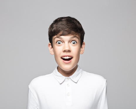 Portrait of surprised teenage boy with mouth open standing against gray background.