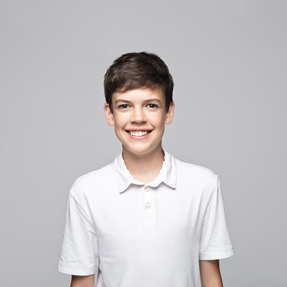 Portrait of happy teenage boy in t-shirt standing against gray background.