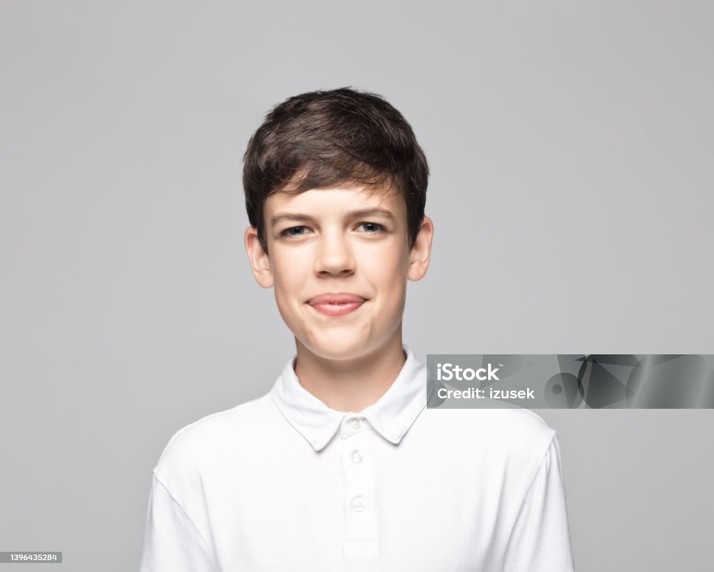 Smiling teenage boy over gray background Portrait of smiling teenage boy wearing t-shirt standing against gray background. Teenager Stock Photo