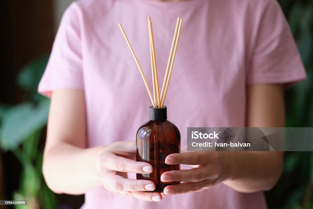 Woman holds jar with an aromatic diffuser of homemade fragrance in hands Woman holds jar with an aromatic diffuser of homemade fragrance in hands. Incense sticks and aromatherapy concept Aromatherapy Diffuser Stock Photo