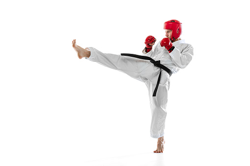 Portrait of young sportive man wearing white dobok, helmet and gloves practicing isolated over white background. Concept of sport, education, skills, workout, health. Copy space for ad