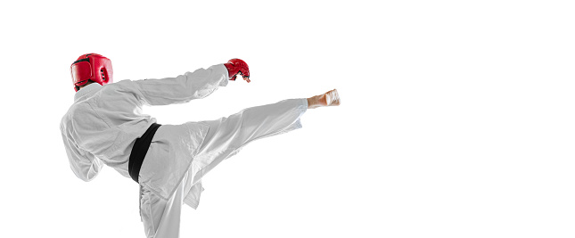 Back view. Portrait of young sportive man wearing white dobok, helmet and gloves practicing isolated over white background. Concept of sport, education, skills, workout, health. Copy space for ad