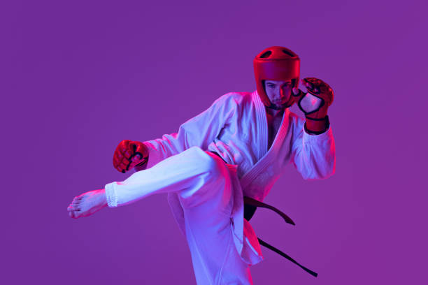 scatto in studio di combattente maschile di taekwondo in uniforme sportiva in azione isolato su sfondo viola in luce al neon. concetto di sport, allenamento, competizione, pubblicità - purple belt foto e immagini stock