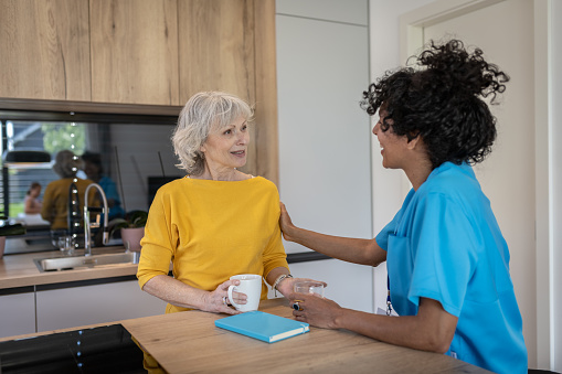 A Latin nurse conducts an interview with a patient at home in a happy mood over coffee.