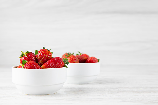 Fresh ripe strawberries in a white bowl on a white wooden background