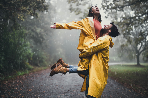 Carefree woman having fun while being held by her boyfriend on a rain in nature. Copy space.