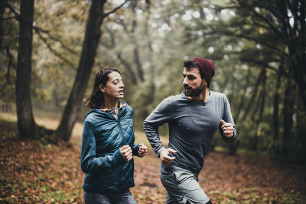 istock Young athletic couple running during cold day in the forest. 1396438100