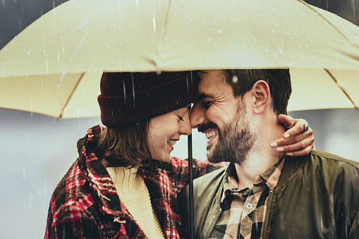 Young affectionate couple enjoying in their love during rainy day under the umbrella.