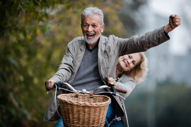 秋の日に自転車で楽しんでいる遊び心のあるシニアカップル。 - retirement mature couple couple bicycle ストックフォトと画像