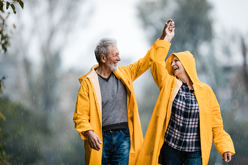 Happy senior couple holding hands and having fun while dancing on rain at the park.