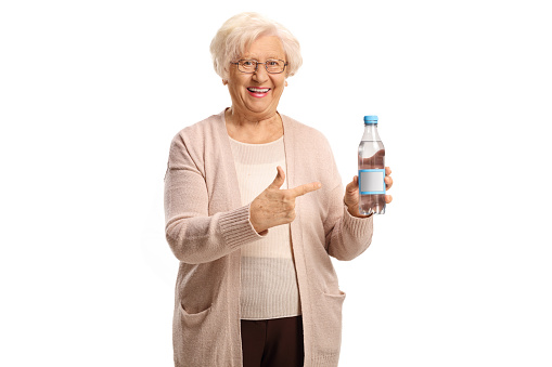 Elderly woman holding a plastic bottle of water and pointing isolated on white background